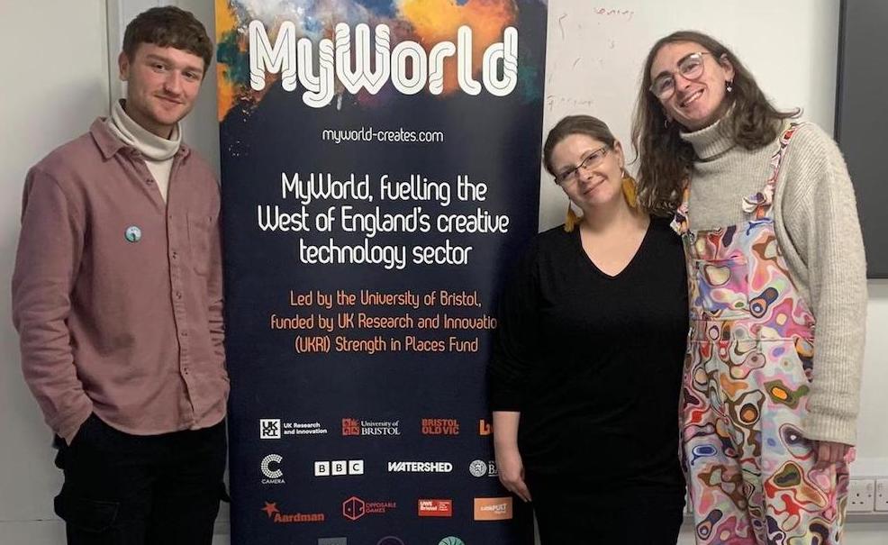 Three people standing by a MyWorld banner