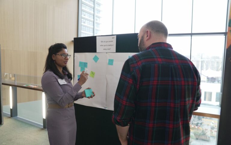 Two people talking and adding post-it notes to a board