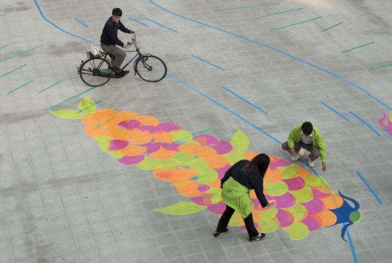 A colourful fish painted on the ground as people interact with the art.