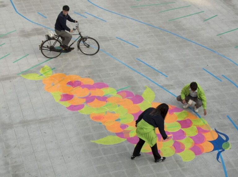 A colourful fish painted on the ground as people interact with the art.
