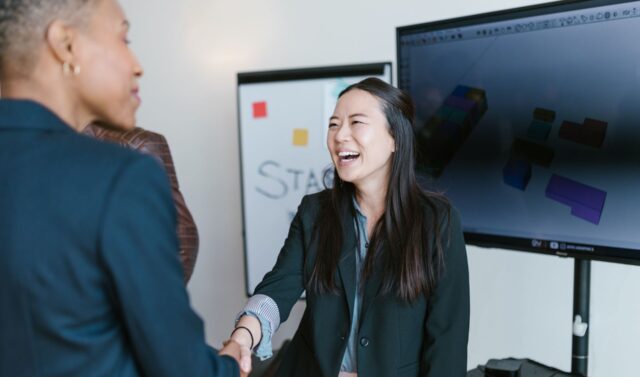 An image of two women shaking hands smiling.