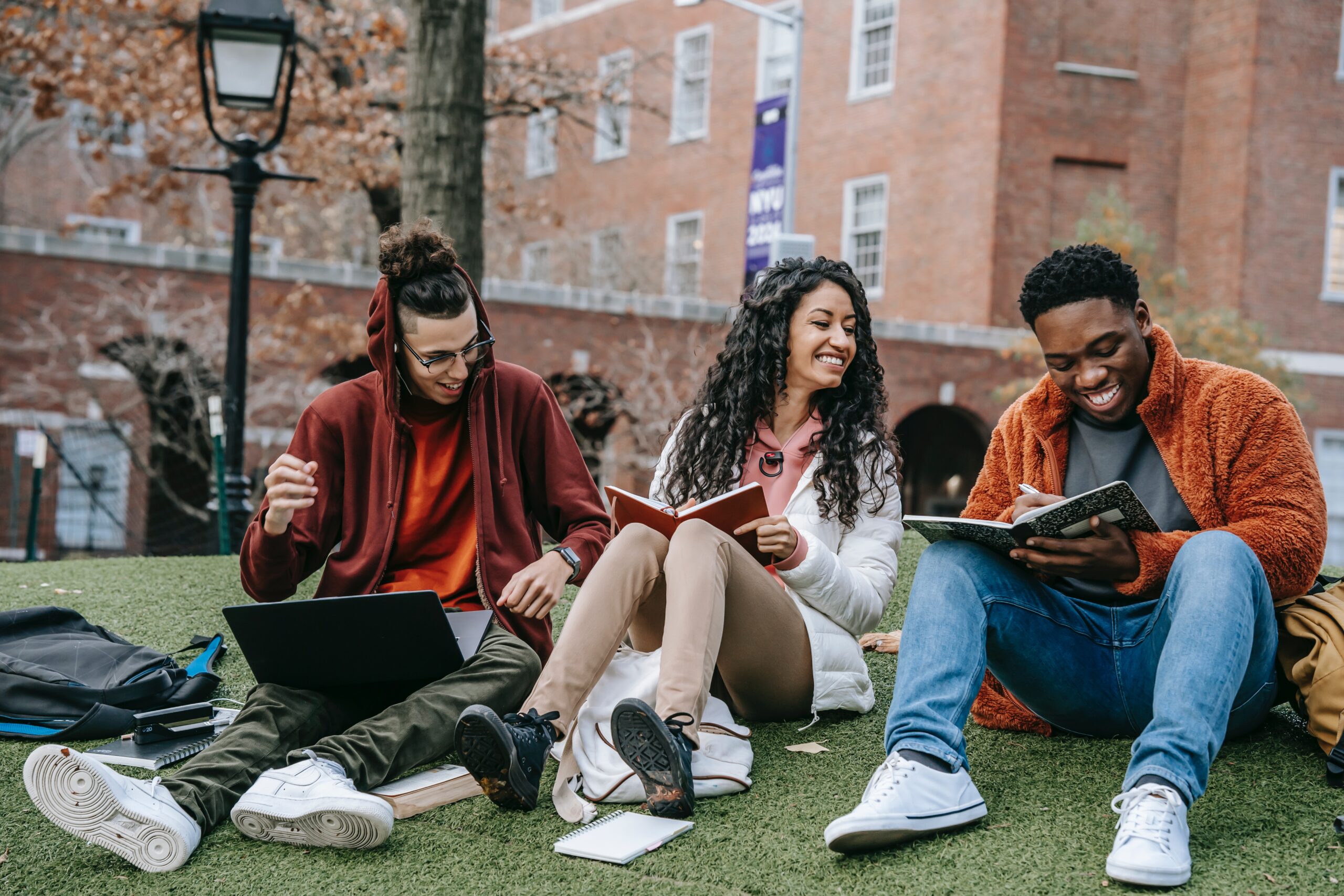 3 young adults studying and smiling outside a red brick building