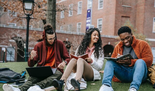 A group of people sat on a hill with books in hands laughing together.