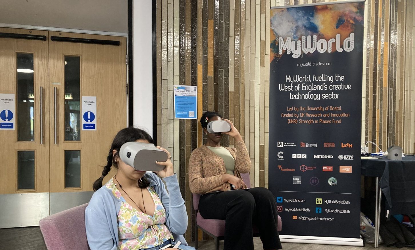 2 girls wearing a vr headset in front of MyWorld banner