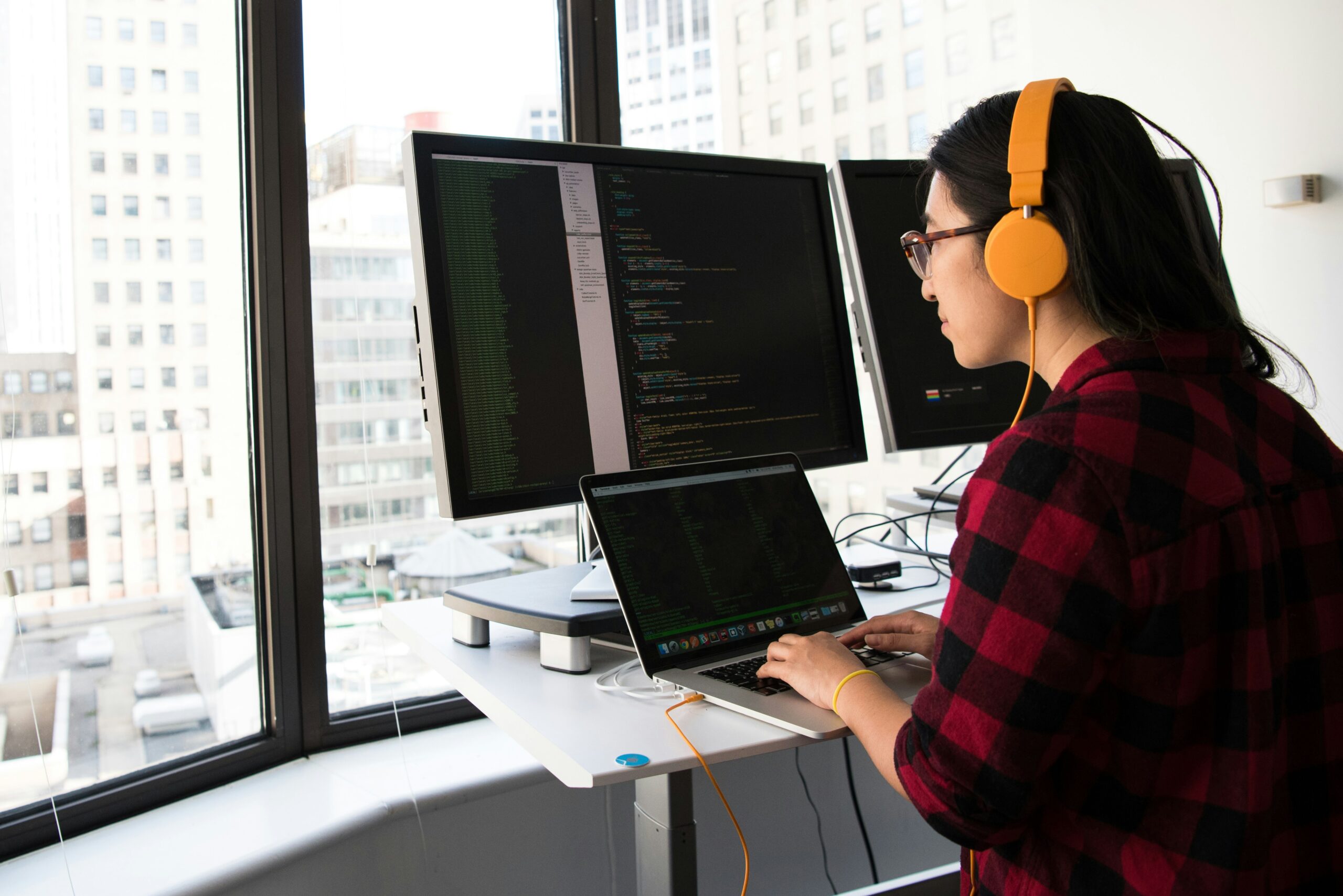 woman using a laptop and multiple screens with code