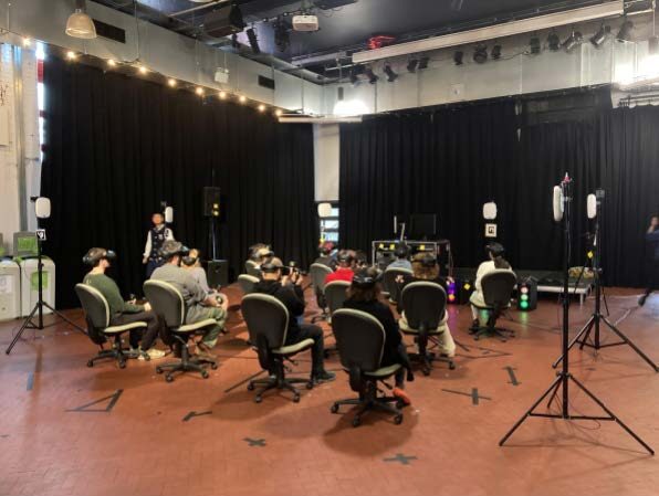 An image of 12 people sat in chairs, with VR headsets on.