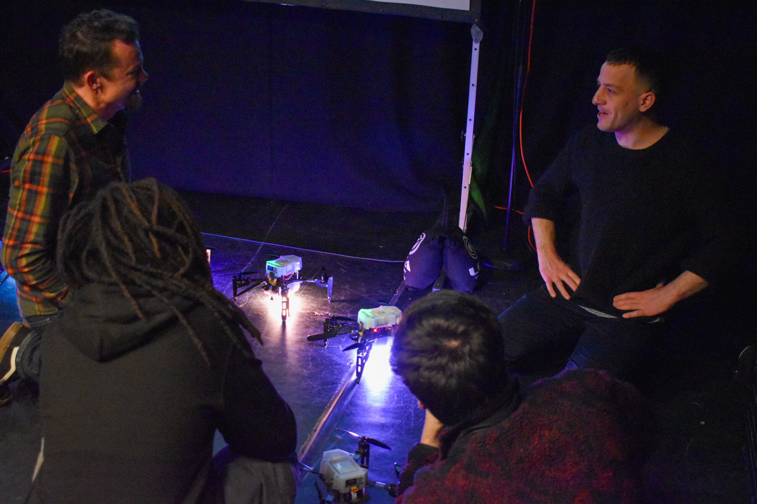 An image of people sat on the floor, surrounded by drones.